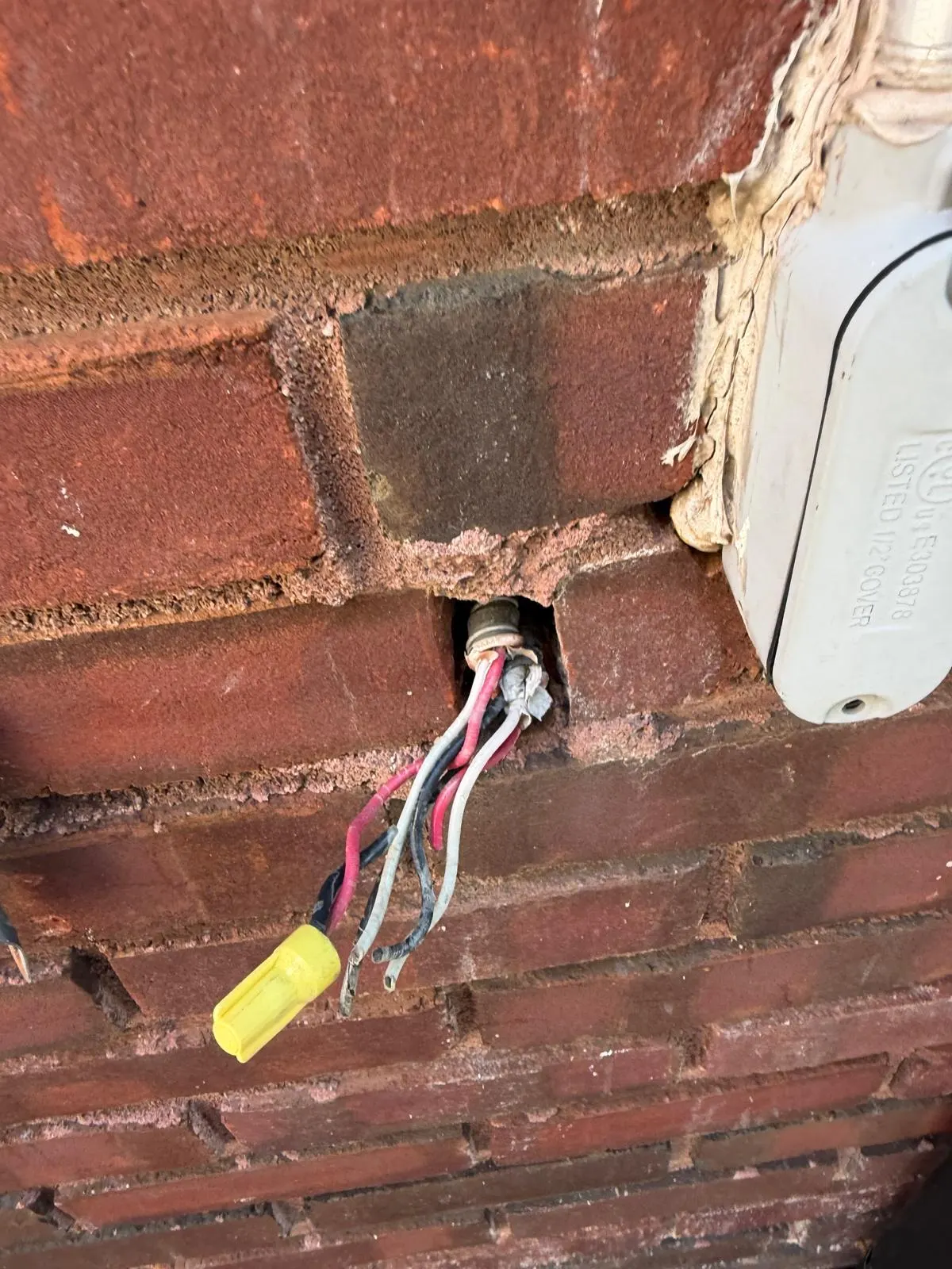 Electrical wiring passing through a hole in a brick wall with a brick missing