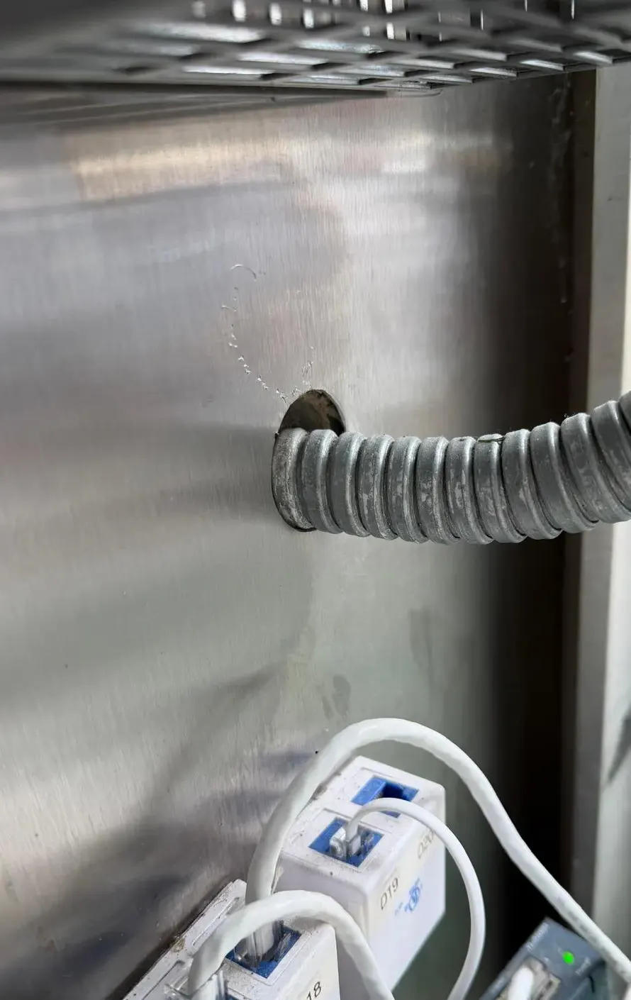 Flexible metal conduit entering an oversized hole in a stainless steel wall panel