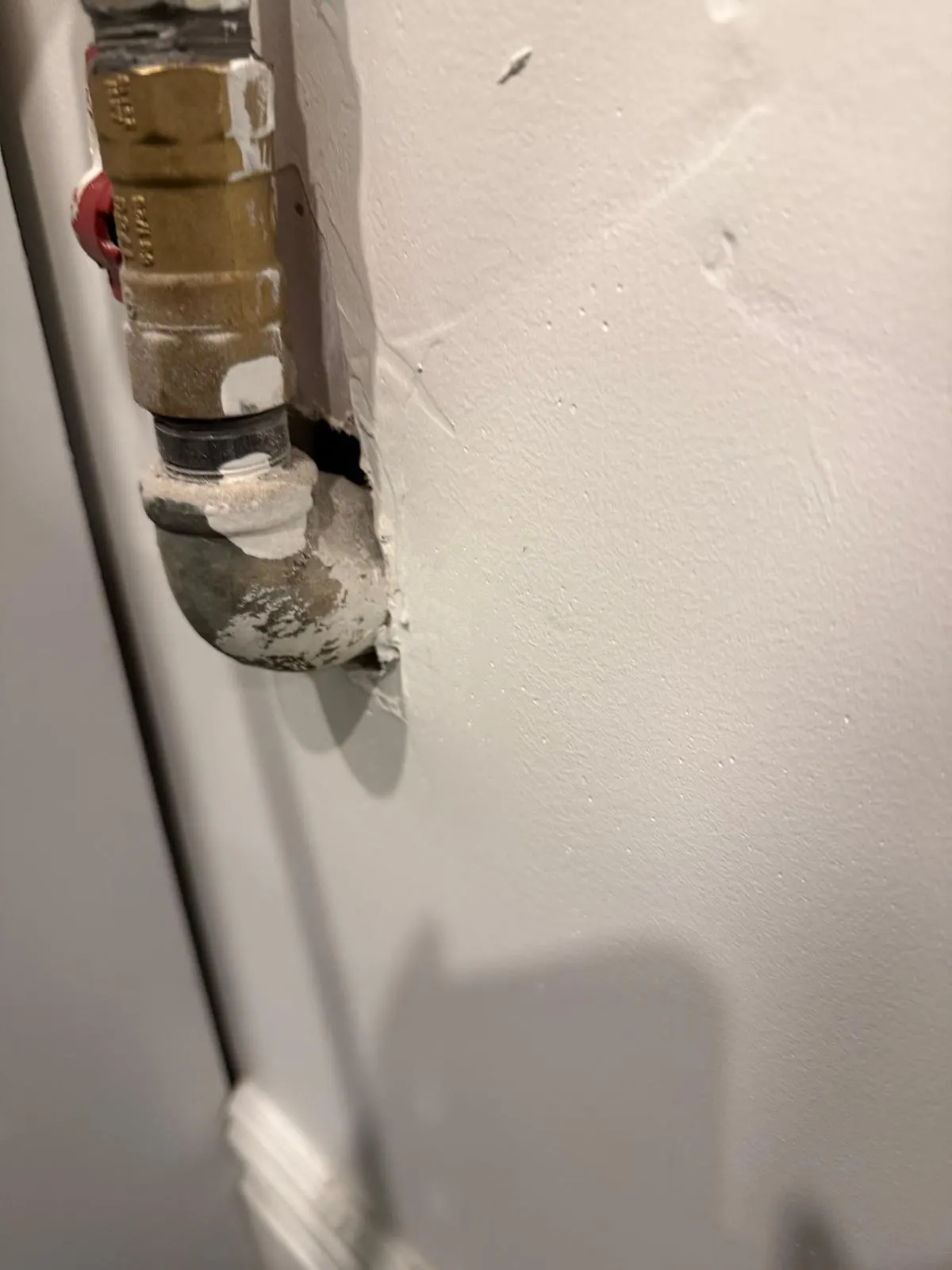 An open gap in drywall around a newly installed pipe and valve