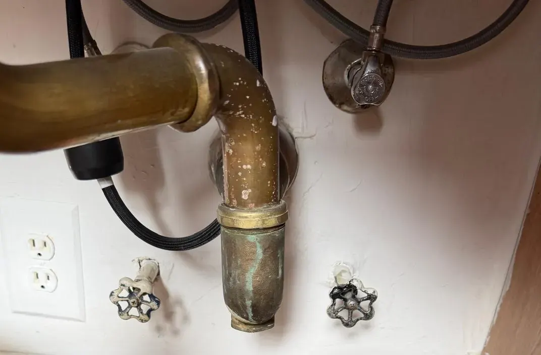 Open gaps in the wall around two shut-off valve stems under a sink