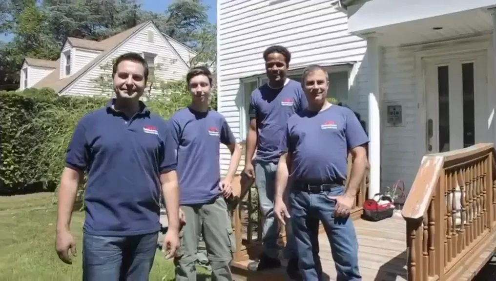 Four Our Exterminator technicians in company shirts outside a customer's house